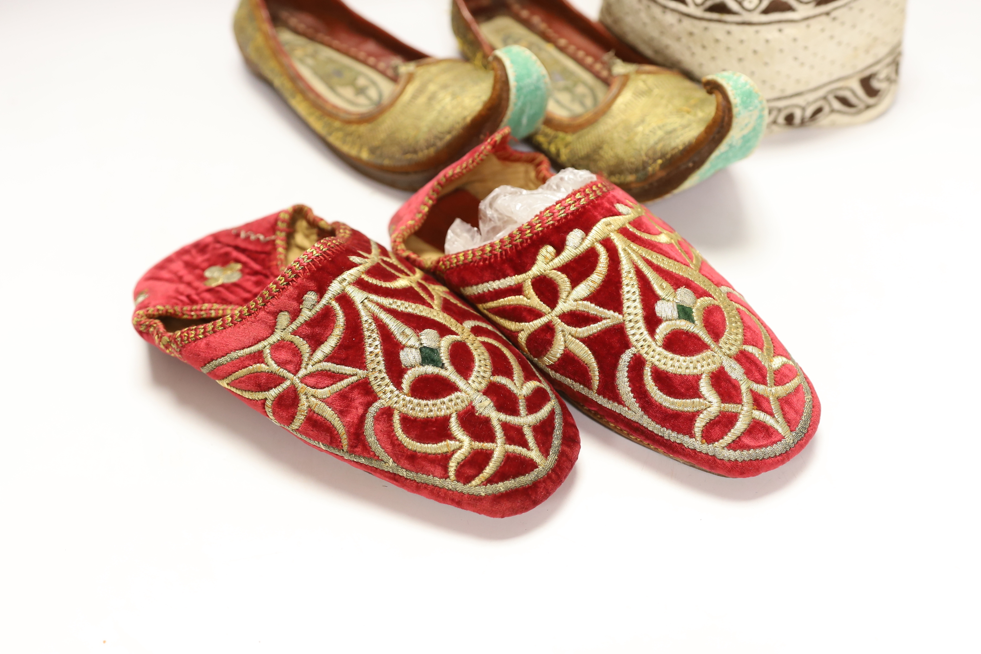 A pair of early 20th century metal thread embroidered Turkish slippers, a pair of similar embroidered red velvet children’s Indian slippers, an embroidered chain stitch drawstring purse and a quilted child’s hat